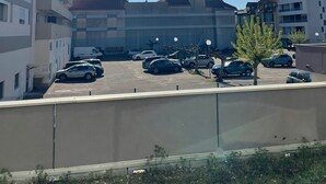 Un estacionamiento con varios autos, un edificio grande de varios pisos y un cielo azul despejado.