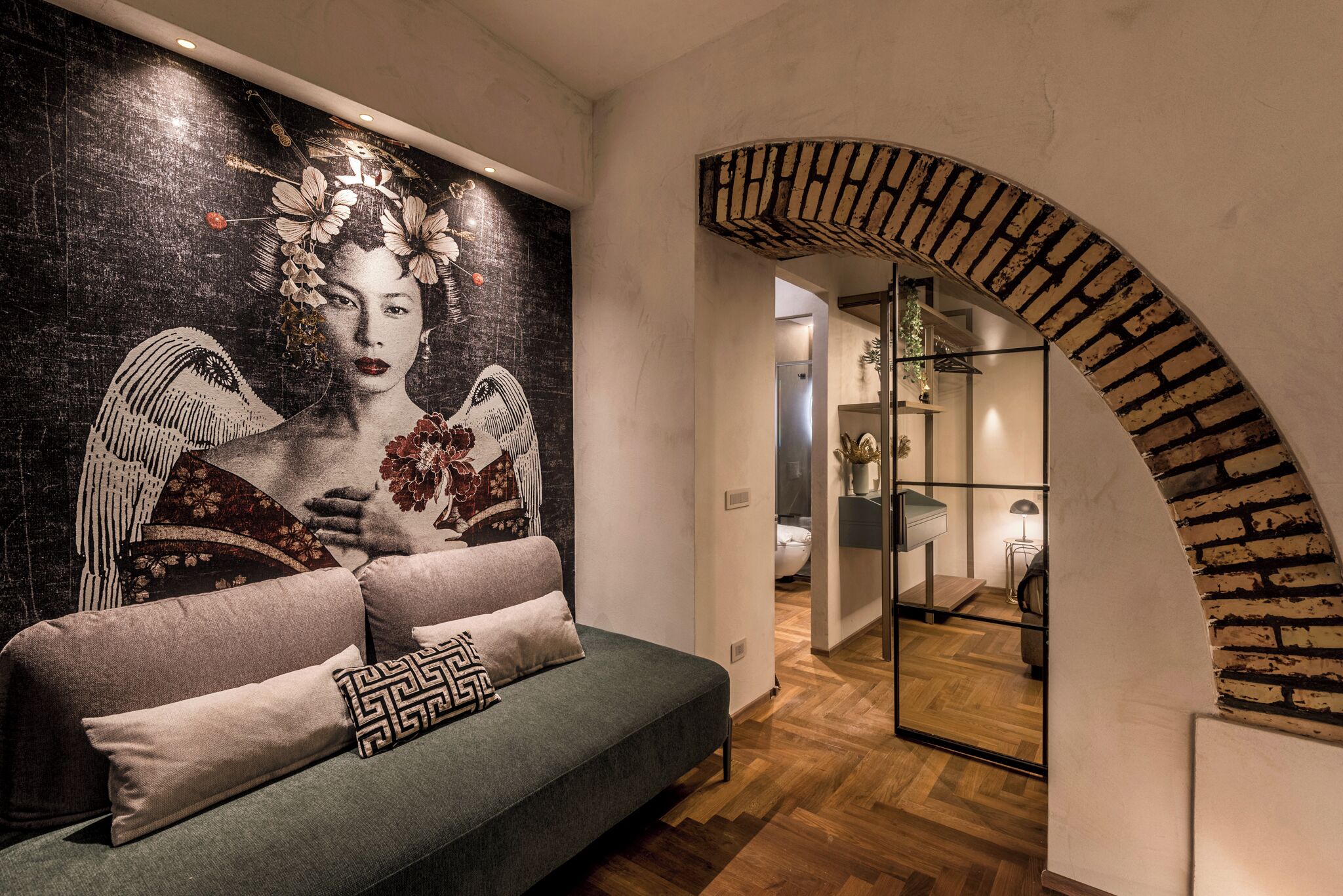 A modern interior with a sofa, a large mural, and a brick archway leading to another room.