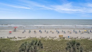 A beach with a lifeguard tower, beach umbrellas, and a sandy area with sparse vegetation. - Cozy condo in wonderful Myrtle Beach with refreshing AC (Myrtle Beach)