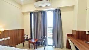 A hotel room with a bed, a desk, a chair, a table, and a window with curtains. - Hotel Krishna Anandam Regency (Vrindavan)