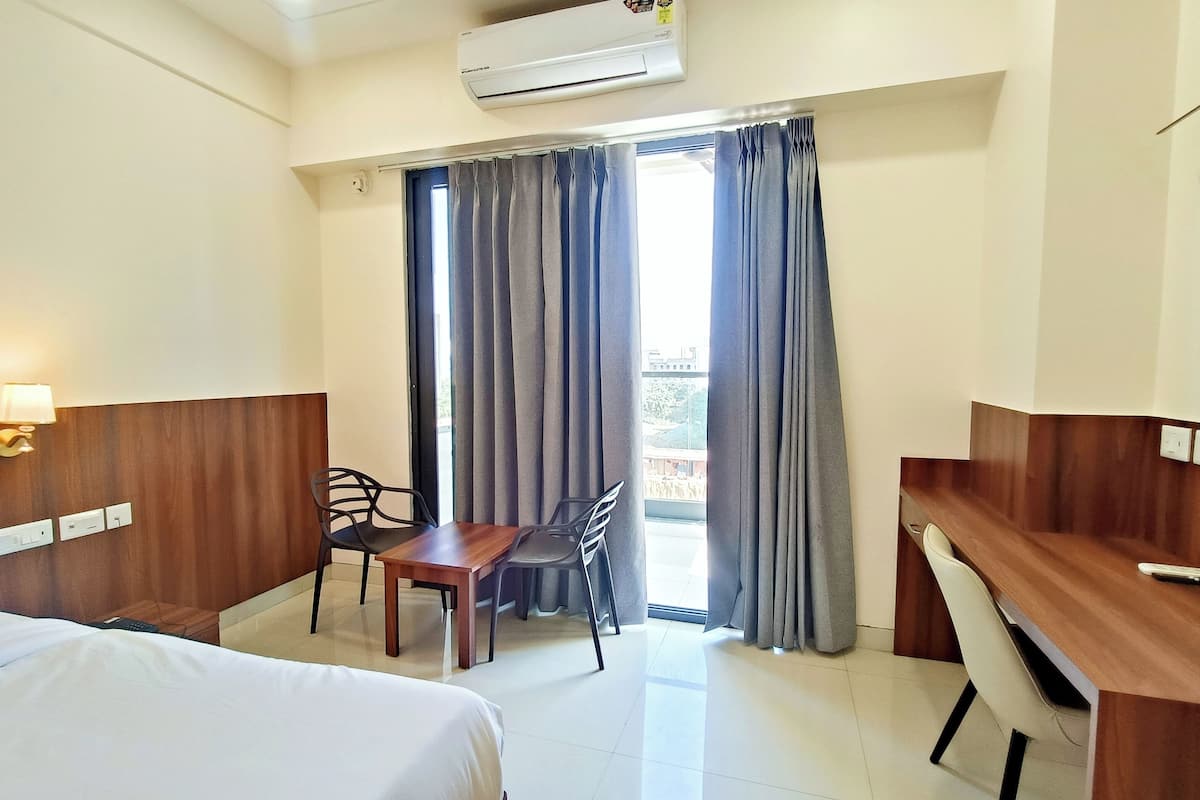 Une chambre d’hôtel avec un lit, un bureau, une chaise, une table et une fenêtre avec des rideaux.