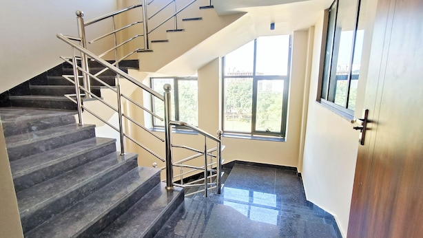 A modern interior with a marble staircase, metal railings, and large windows allowing natural light. - Hotel Krishna Anandam Regency (Vrindavan)