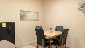 Ein kleiner, privater Essbereich mit einem Tisch und vier Stühlen, einem Wandventilator und einem Kühlschrank mit Wasserspender.