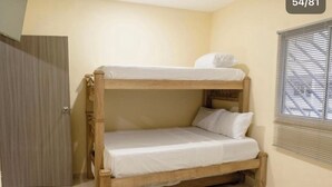 Ein Stockbett mit weißer Bettwäsche in einem Zimmer mit beigen Wänden und einem Fenster mit Jalousien.