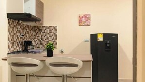 Eine kleine Küche mit zwei Barhocker, einem schwarzen Kühlschrank, einer gefliesten Spritzschutzwand und einem kleinen Topfpflanzen.