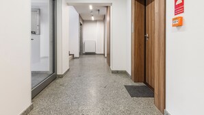 A hallway with a wooden door, a sign indicating a room for the hearing impaired, and a radiator in the distance. - Lumina Family apartment with patio (Warsaw)