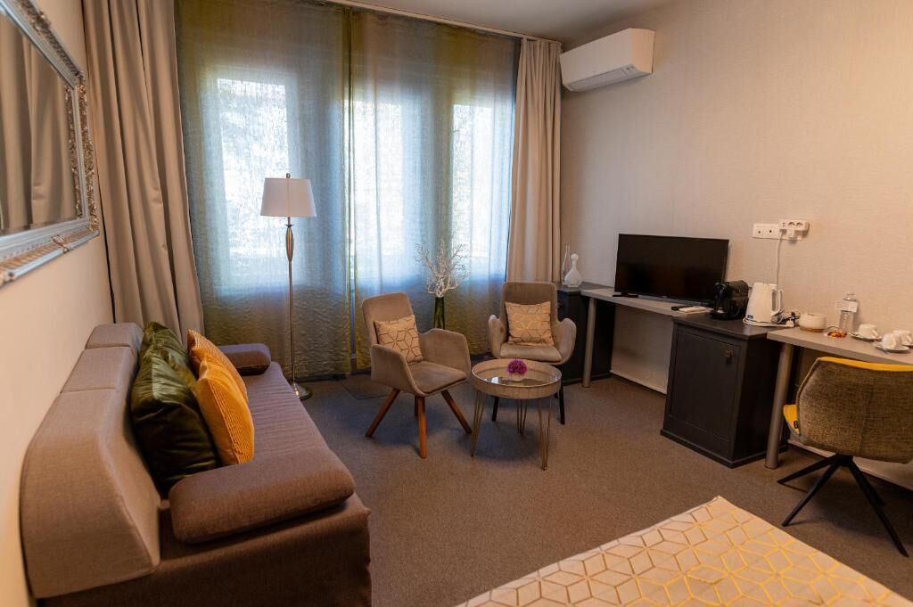 A compact living space with a sofa, two armchairs, a small coffee table, a TV, and a kitchenette area.