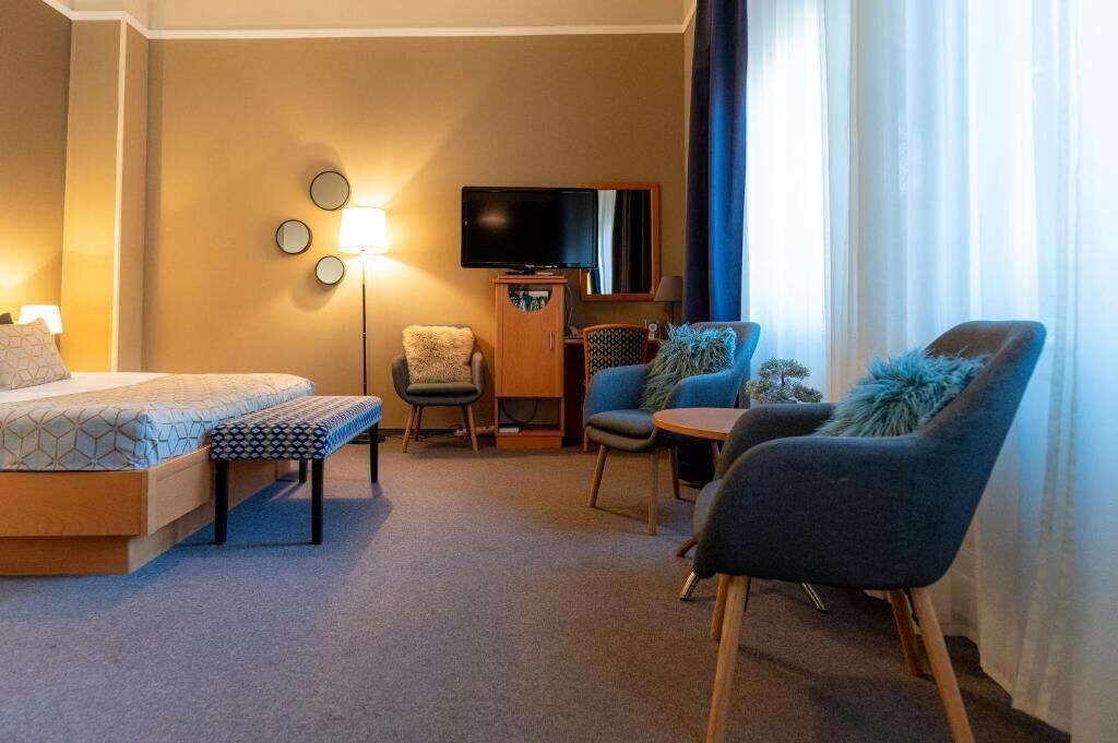 A hotel room with a bed, a desk, a chair, a sofa, a TV, and a lamp.