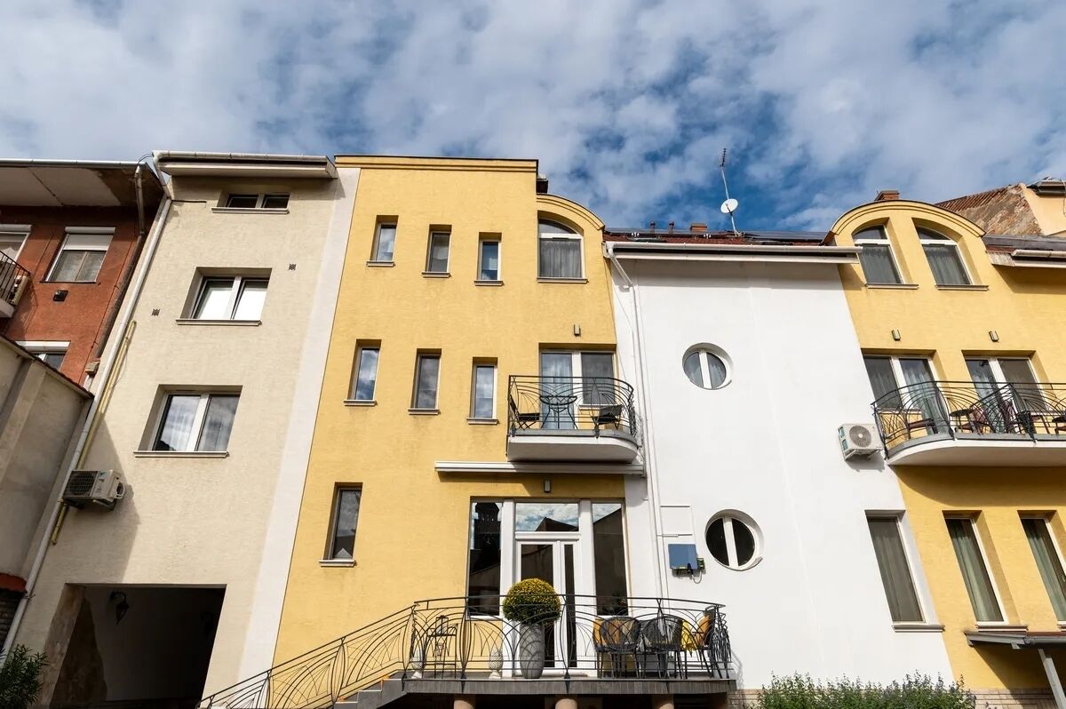 Un edificio residencial de varios pisos con balcones, una entrada central y cielo despejado.