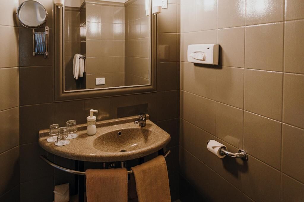Une salle de bain équipée d’un lavabo, d’un miroir, d’un porte-serviettes et d’un sèche-mains.