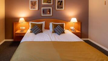 Een hotelkamer met een groot bed, twee nachtkastjes met lampen, en ingelijste foto’s aan de muur.