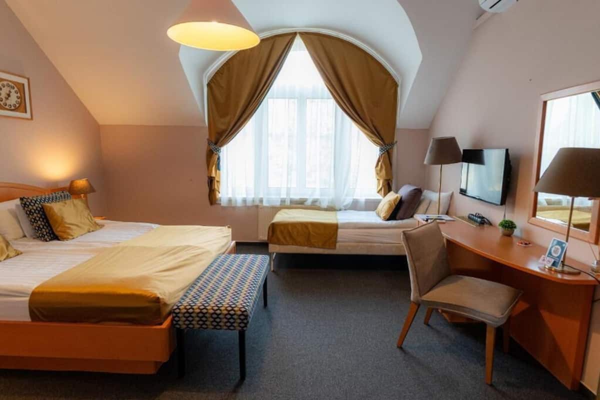 Hotellihuone, jossa on kaksi sänkyä, työpöytä, tuoli, televisio ja suuri ikkuna, jossa on verhot.