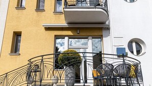 Un edificio amarillo con balcón, una planta en maceta y asientos al aire libre.
