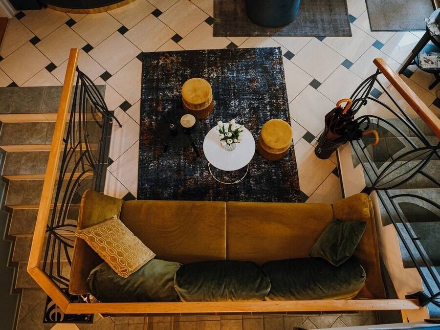 A high vantage point view of a room with a brown sofa, a round table with a white plate and two yellow cushions, and a pair of shoes on a chair.