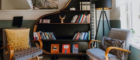 A living room with a grand piano, two patterned chairs, a bookshelf, and a floor lamp.
