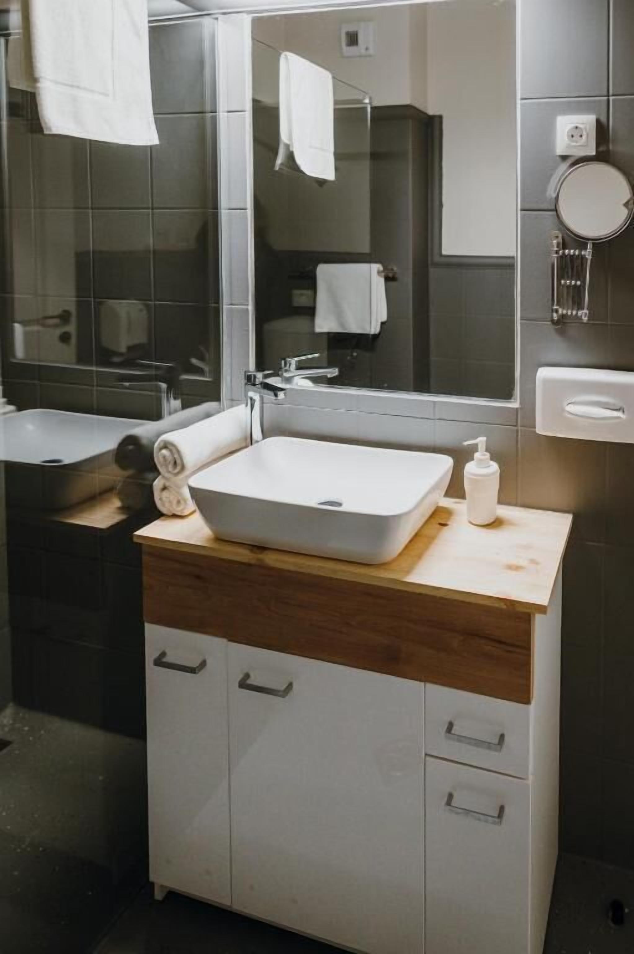 A modern bathroom with a large mirror, white sink, and wooden vanity.