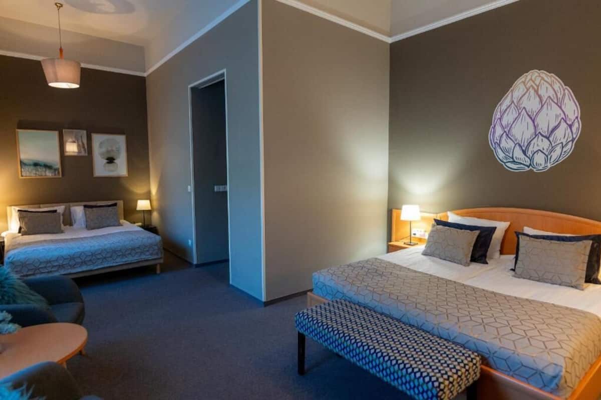 Hotellihuone, jossa on kaksi sänkyä, penkki, pieni pöytä ja seinätaidetta.