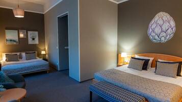 A hotel room with two beds, a bench, a small table, and wall art.