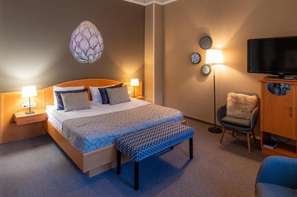 A hotel room with a bed, bedside lamps, a television, a chair, and a wall decoration.
