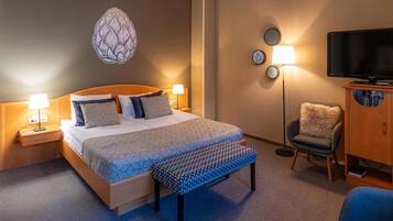 A hotel room with a bed, bedside lamps, a television, a chair, and a wall decoration.