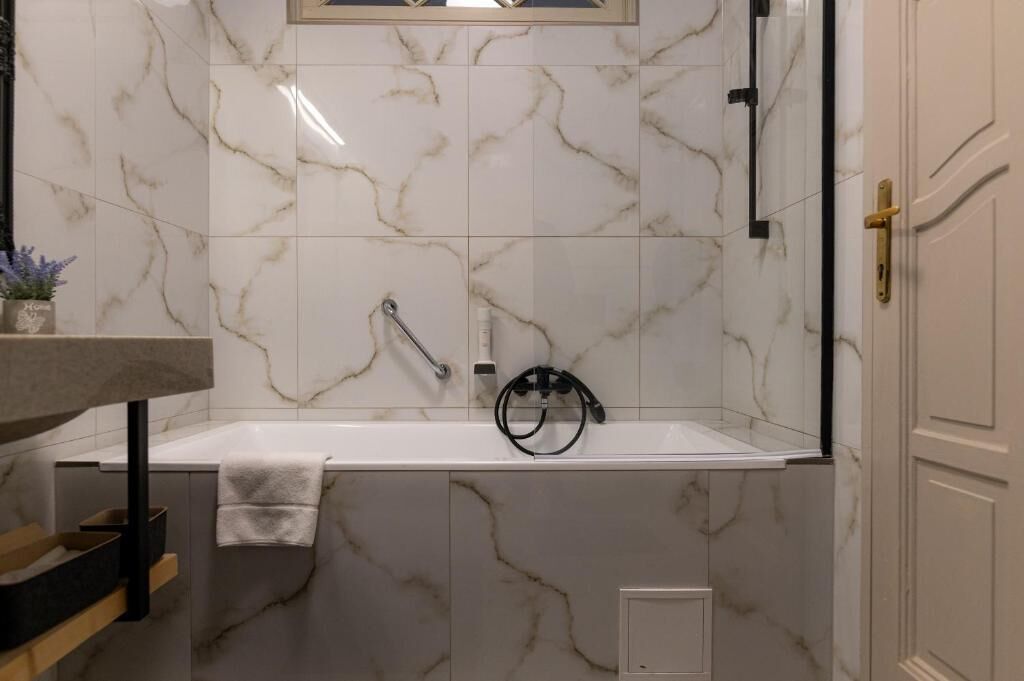 A bathroom with a marble wall, a bathtub, a towel rack, and a door with a gold handle.