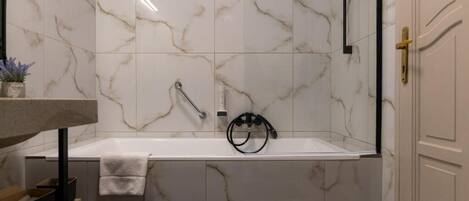 A bathroom with a marble wall, a bathtub, a towel rack, and a door with a gold handle.