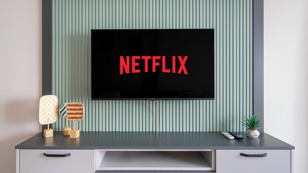 Un meuble de divertissement moderne doté d’un téléviseur à écran plat affichant le logo « NETFLIX », d’une télécommande et d’objets décoratifs.