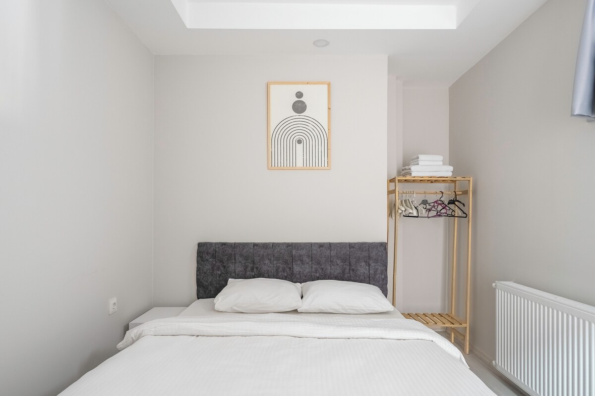 Une chambre avec un lit, une œuvre d’art accrochée au mur, un radiateur et un étendoir en bois.