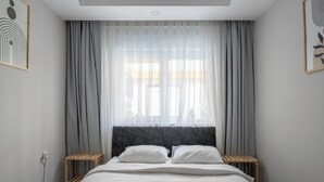 Un lit bien fait, avec une tête de lit, deux tables de chevet et des rideaux légers.