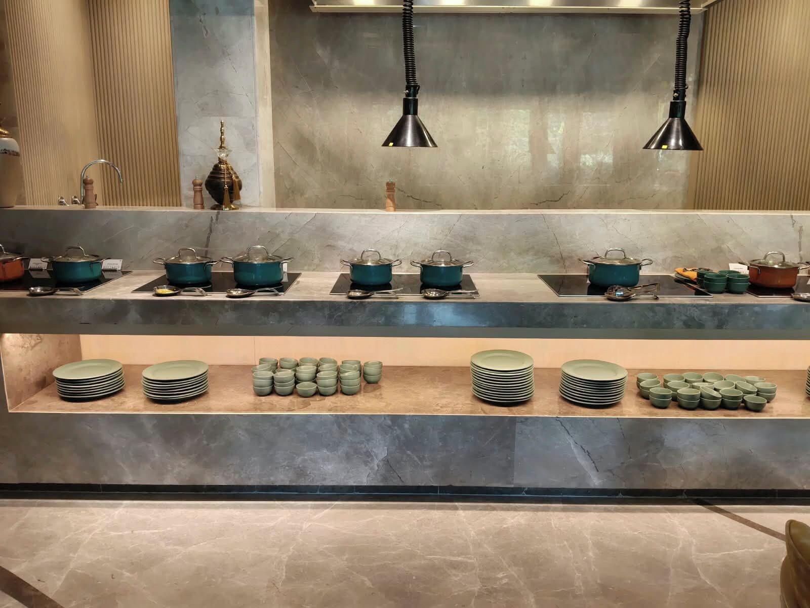 Un área de cocina con múltiples estaciones de cocina, cada una equipada con ollas y sartenes, y una variedad de platos y tazones.