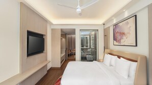 A modern hotel room with a large bed, a flat-screen TV, a ceiling fan, a glass shower, and a bathroom with a mirror. - Hotel Gwalior Regency, a member of Radisson Individuals (Gwalior)