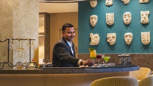 A bar area with a bartender, a counter with glasses, a drink, and decorative masks on the wall. - Hotel Gwalior Regency, a member of Radisson Individuals (Gwalior)