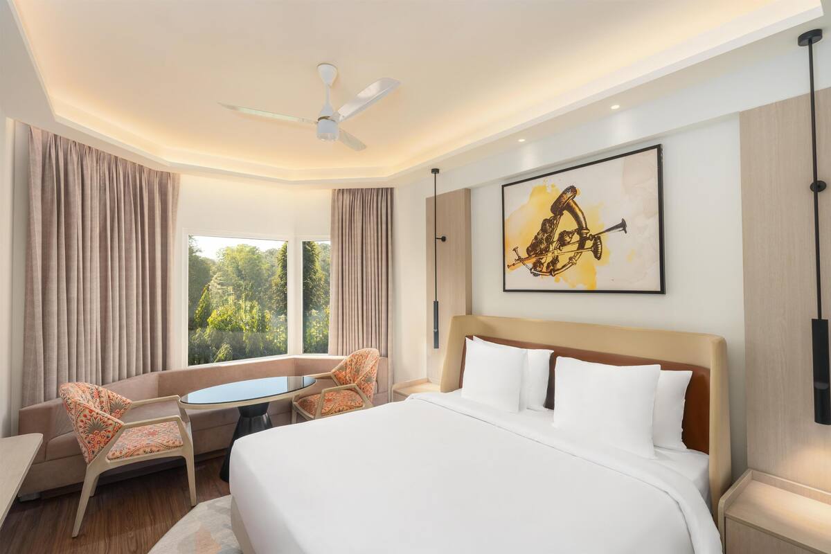 A hotel room with a bed, a chair, a table, and a large window with curtains.