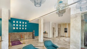 A lobby with teal chairs, a marble floor, and a wall with various shapes. - Hotel Gwalior Regency, a member of Radisson Individuals (Gwalior)