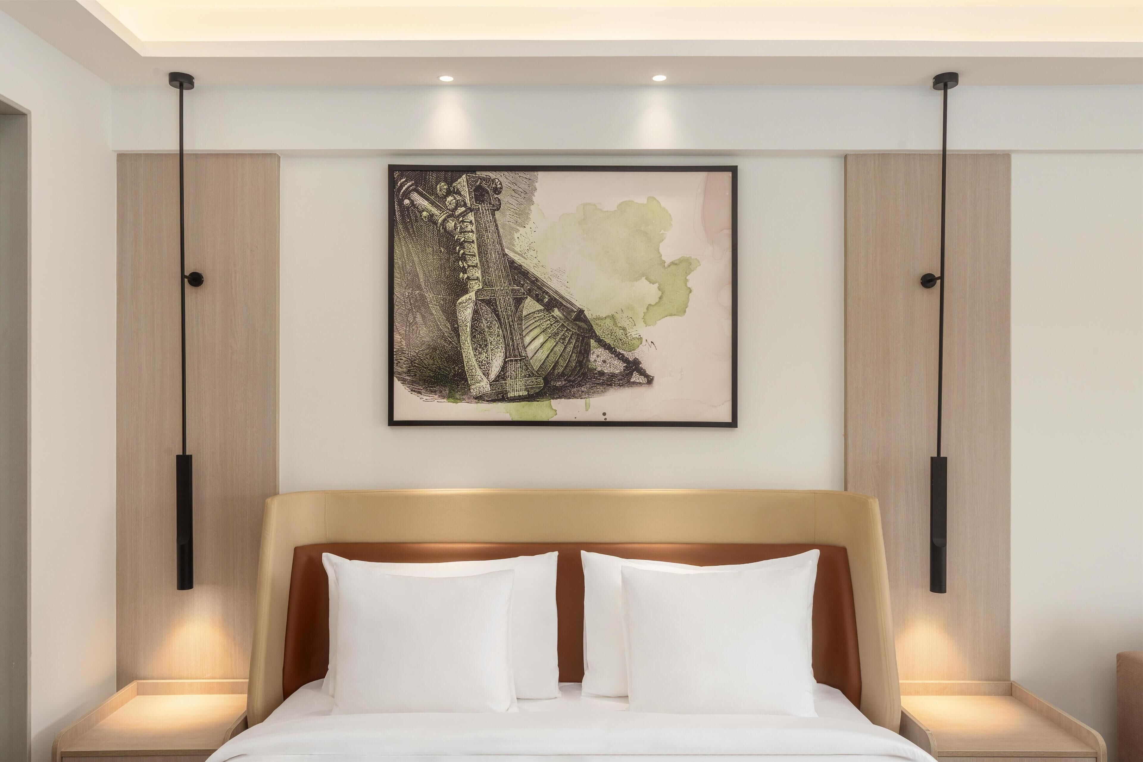 A modern hotel room with a large bed, two bedside tables, and a framed artwork above the bed.