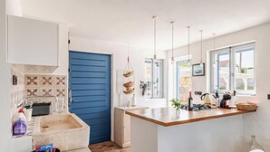 A modern kitchen with a blue door, white cabinets, and a large island with a sink and stove. - Secluded stone villa with private pool on peaceful Solta Island (Gornje Selo)
