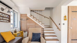 A modern living room with a beige sofa, a small armchair, a wooden staircase, and a wooden door. - Secluded stone villa with private pool on peaceful Solta Island (Gornje Selo)