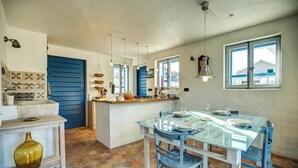 A kitchen with a blue door, a central island, hanging pendant lights, and a dining area with a glass table and blue chairs. - Secluded stone villa with private pool on peaceful Solta Island (Gornje Selo)