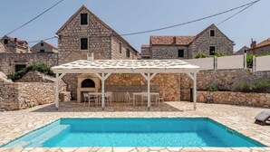 A stone pool with a pergola and outdoor seating, surrounded by stone buildings. - Secluded stone villa with private pool on peaceful Solta Island (Gornje Selo)