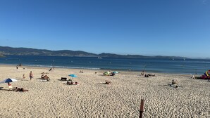 A beach with people sunbathing and swimming, a clear sky, and distant hills. - Luxury suite in charming B&B in Galicia (O Agro)