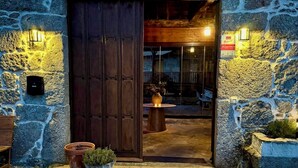A stone building with a wooden door, potted plants, and a small table with a vase. - Luxury suite in charming B&B in Galicia (O Agro)