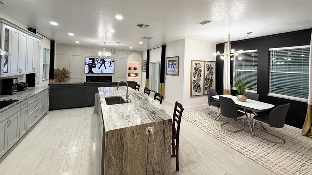 A modern kitchen with a marble island, white cabinets, and a dining area with a table and chairs. - Brand New Luxury Modern 5BR/4.5BA+Game Room Home (Altamonte Springs)