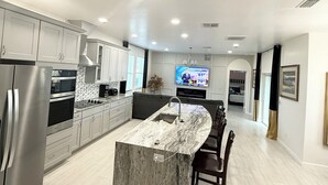 A modern kitchen with stainless steel appliances, a marble island, and a TV in the background. - Brand New Luxury Modern 5BR/4.5BA+Game Room Home (Altamonte Springs)