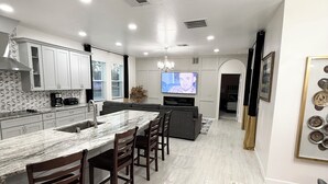 A modern kitchen with a marble countertop, wooden chairs, and a large island. - Brand New Luxury Modern 5BR/4.5BA+Game Room Home (Altamonte Springs)