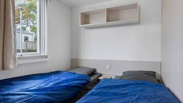 A bedroom with two beds, a window, and a white wall-mounted shelf.
