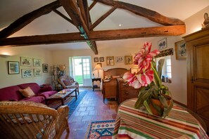 A cozy living room with a high ceiling, wooden beams, a wicker sofa, a patterned rug, and a bed with a striped cover. - A Chateau for all generations. (Saint-Victor-Rouzaud)