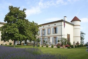 A large, white building with blue shutters, a central tower, and a flagpole. - A Chateau for all generations. (Saint-Victor-Rouzaud)