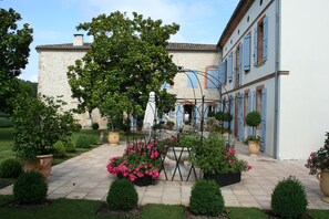 A courtyard with a stone building, potted plants, and a swing set. - A Chateau for all generations. (Saint-Victor-Rouzaud)