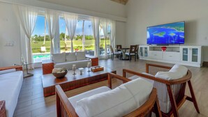 Ein großzügiges Wohnzimmer mit großem Fernseher, bequemen Sitzmöglichkeiten und Blick auf einen Golfplatz.