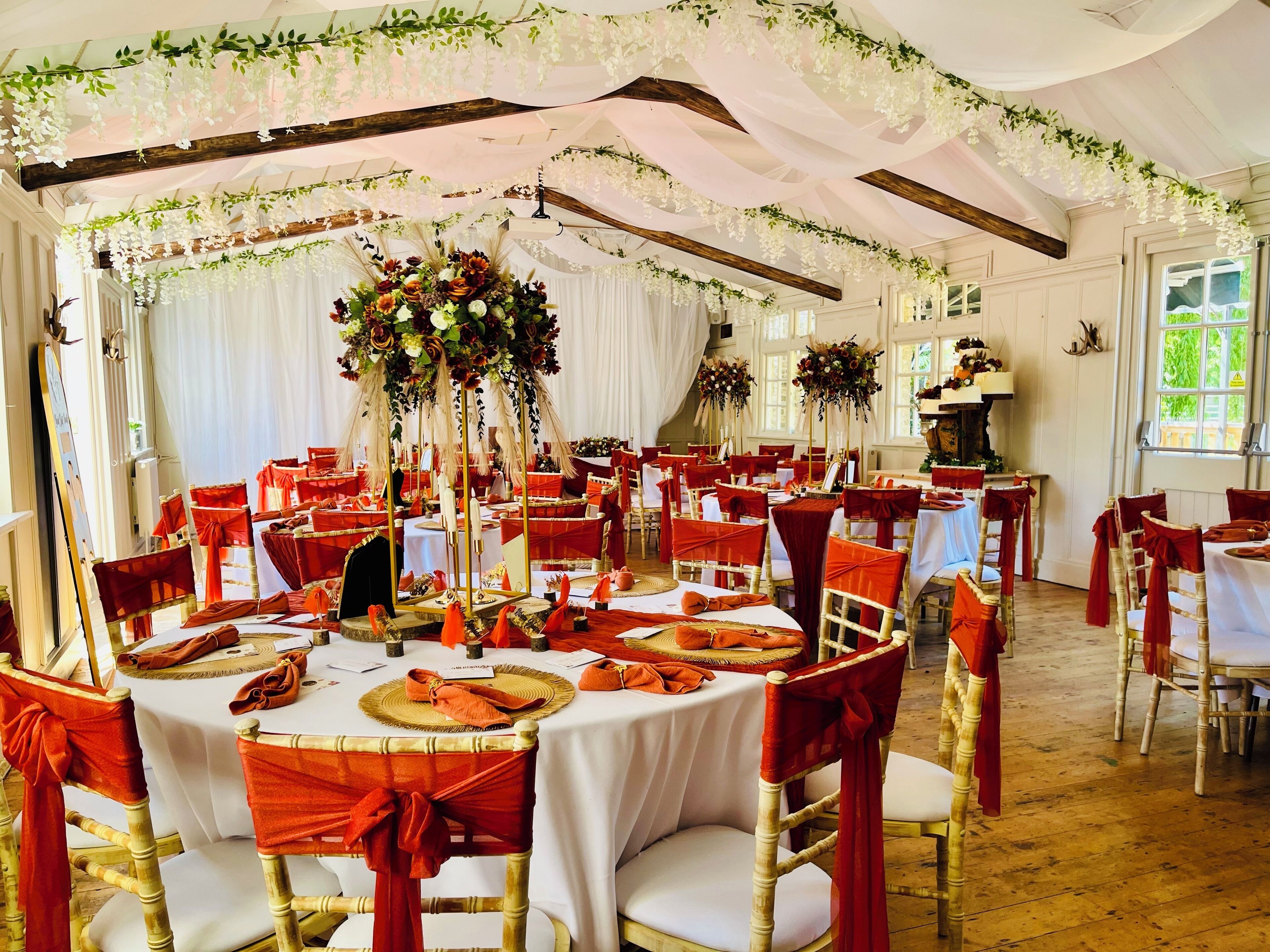 A banquet hall with round tables, red chairs, white tablecloths, and floral centerpieces.